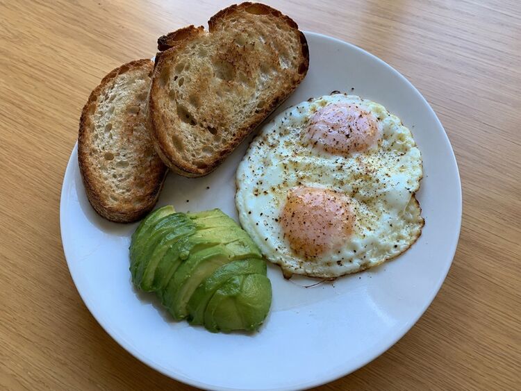 a photo of a plate with two fried eggs, two slices of sourdough toast, and sliced avocado